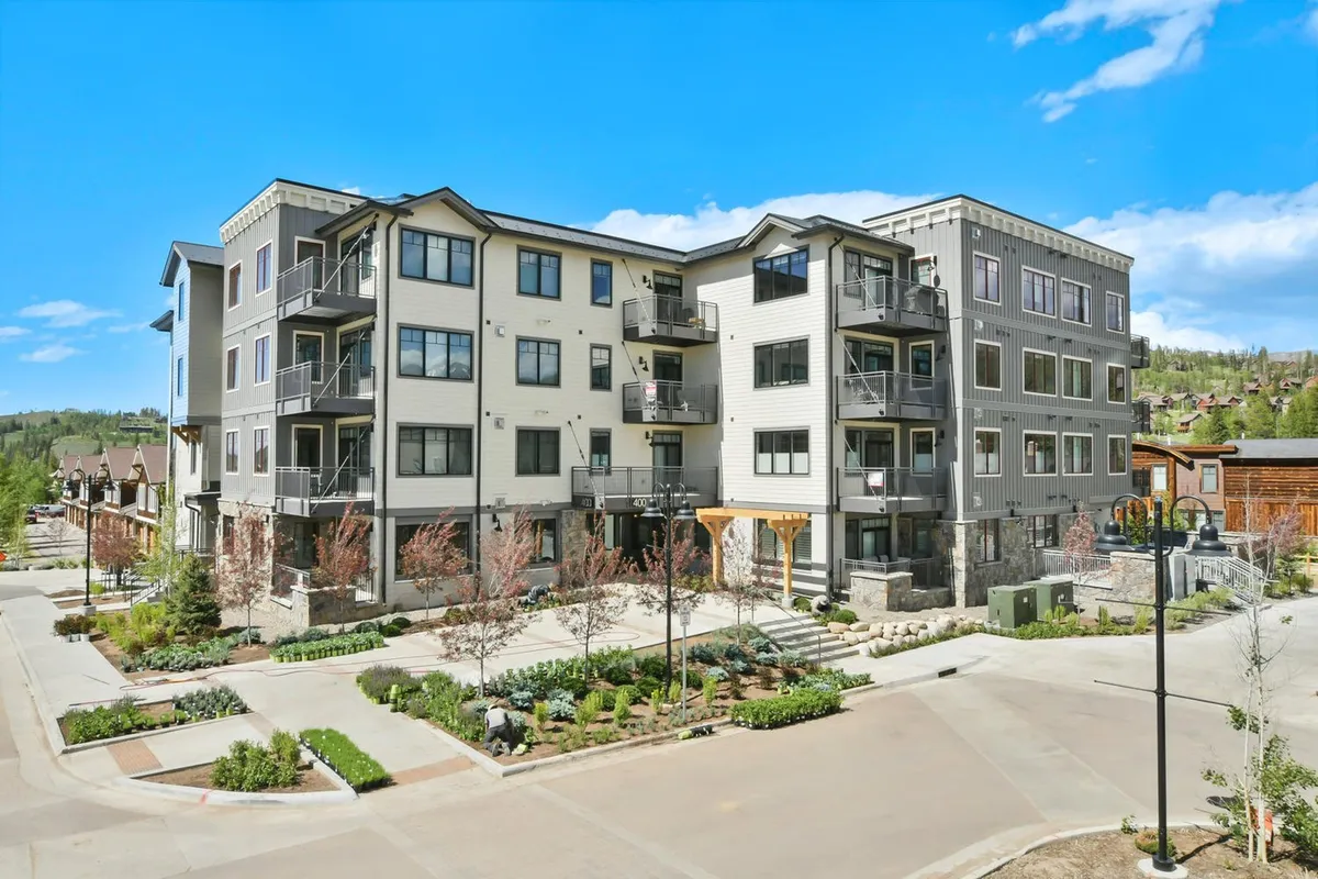 A modern multi-story building is framed by a beautifully landscaped garden with a paved pathway. Residents and guests can be seen relaxing on private balconies, while others enjoy strolls through the lush greenery and socialize in the common outdoor spaces. The building exudes a welcoming and upscale atmosphere, hinting at the luxurious amenities within.