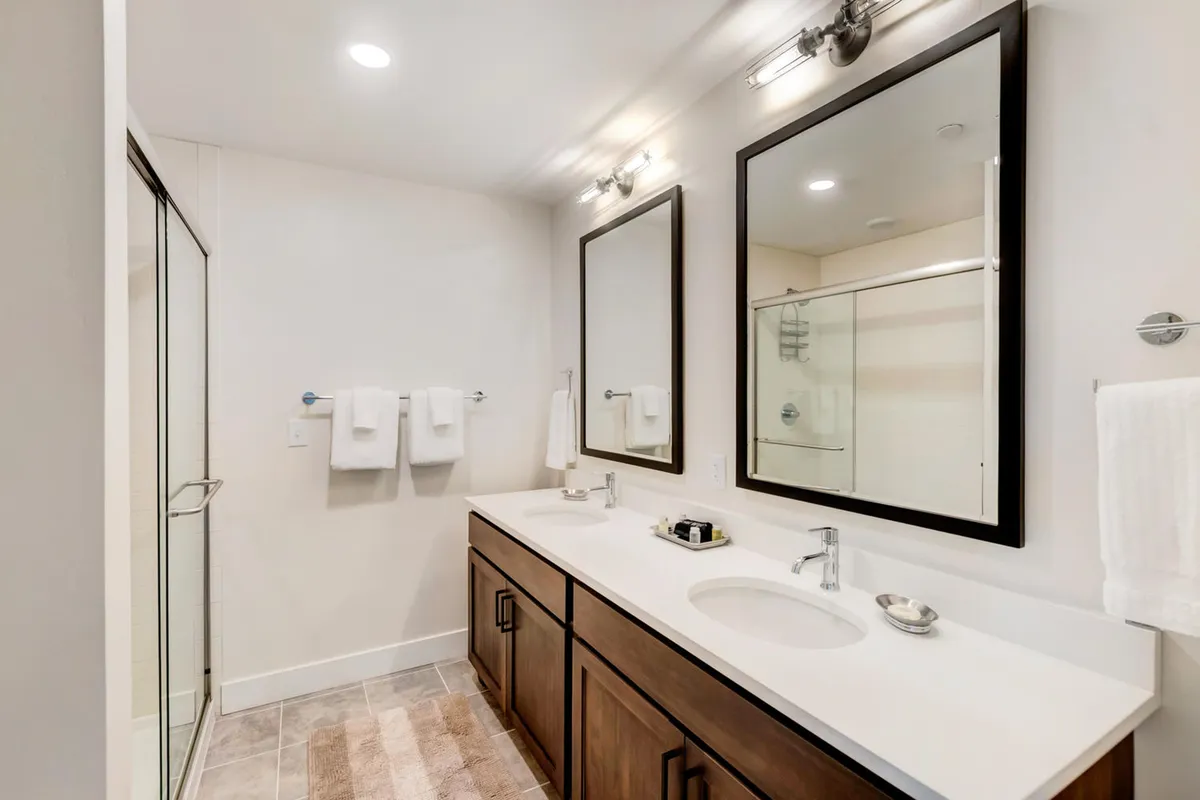 A spa-inspired bathroom with a double vanity, framed mirrors, and a sleek glass shower enclosure. The space exudes calm and modern luxury, ideal for personal grooming and relaxation after an active day.