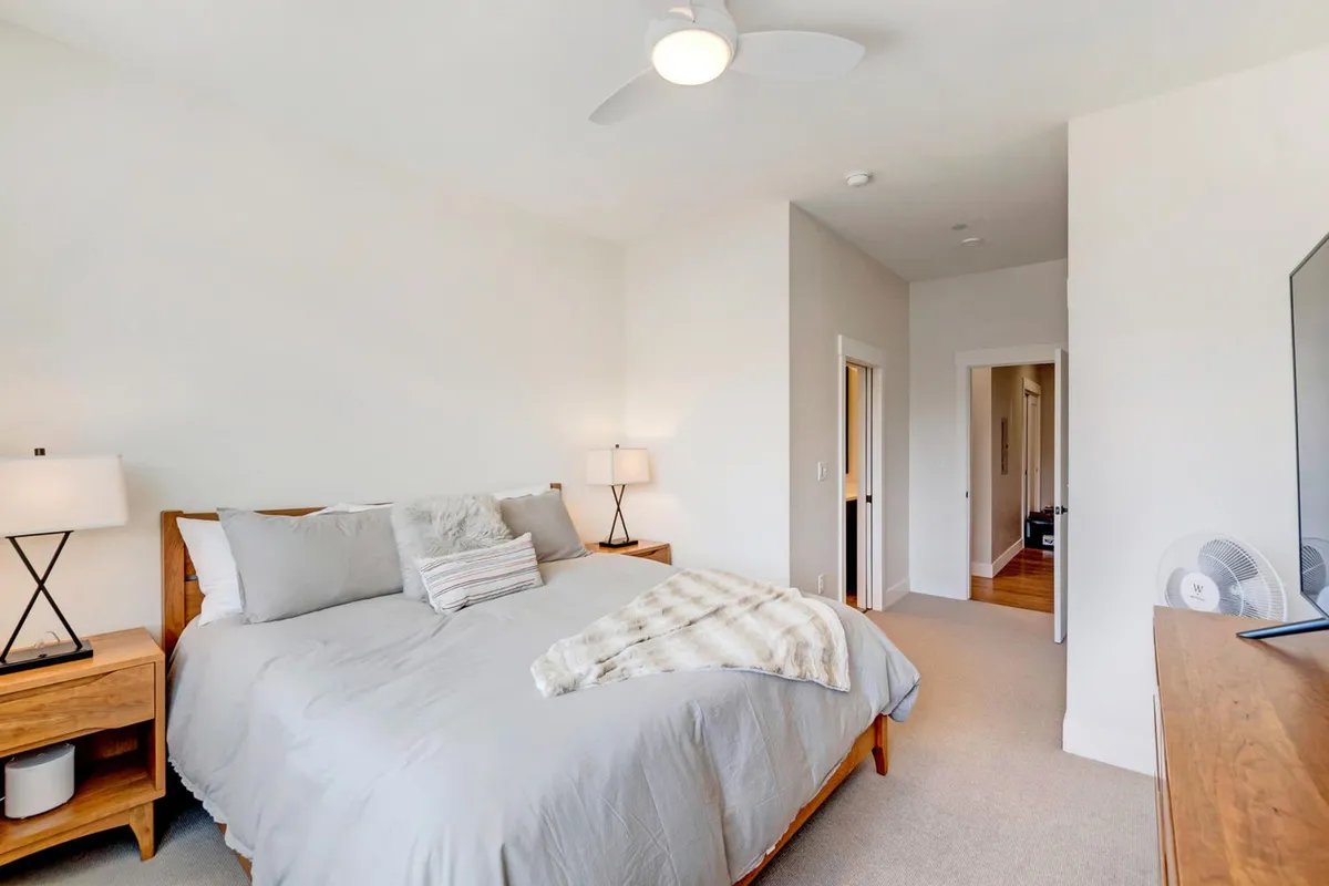 A cozy and tastefully decorated bedroom with a plush bed, nightstands, lamps, and a decorative throw. Soft, natural light bathes the room, highlighting the peaceful atmosphere and attention to detail in the bedding and decor.
