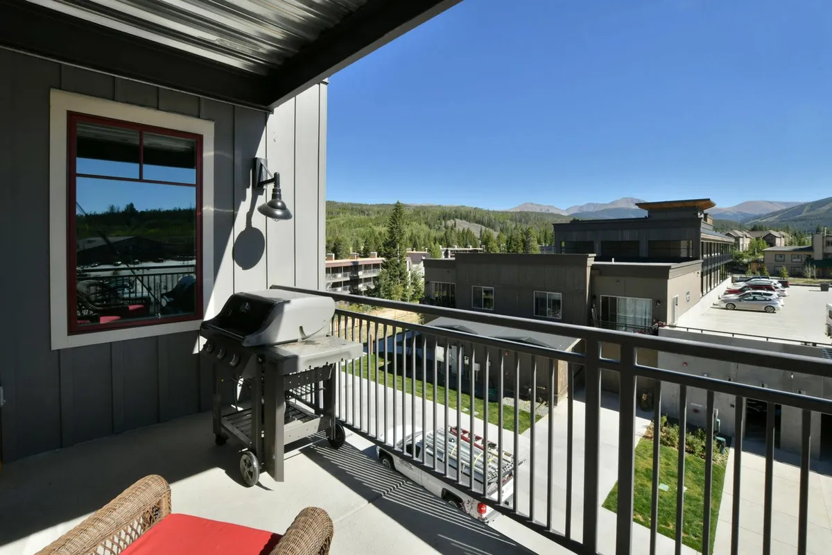 A well-appointed balcony with a grill and a bold red accent chair, overlooking sweeping mountain views. The setup suggests a place for both solo relaxation and shared meals, with scenery that highlights the alpine location.