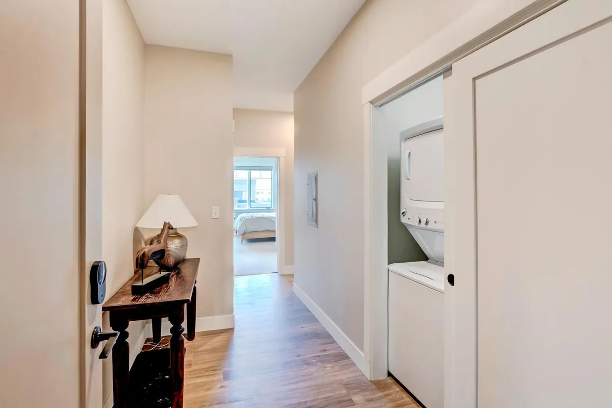 This interior image captures the entrance door, a small table with a lamp, a washer and dryer unit, and a hallway leading to the bedroom. The organized and welcoming scene emphasizes convenience and the feeling of coming home after outdoor adventures.
