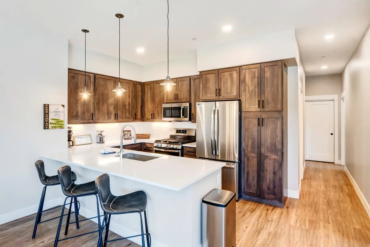 A contemporary kitchen with a central island, stainless steel appliances, wooden cabinetry, and bar stools. The space is designed for cooking and socializing, offering ample room for preparing meals and gathering around the island.