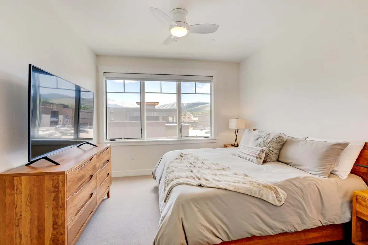 A serene bedroom scene featuring a comfortable bed, a TV, and a window that allows natural light to softly fill the space. The bedding looks plush and inviting, and the overall mood is calm and restful—ideal for unwinding after a day of adventure.