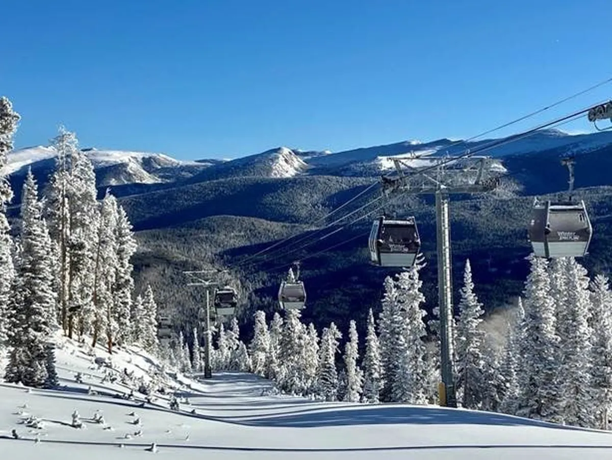 A dramatic exterior shot of snow-covered mountains, ski lift gondolas gliding above frosted trees, and a wide-open blue sky. The scene captures the excitement of alpine activities such as skiing and snowboarding, framed by the natural beauty of the area.