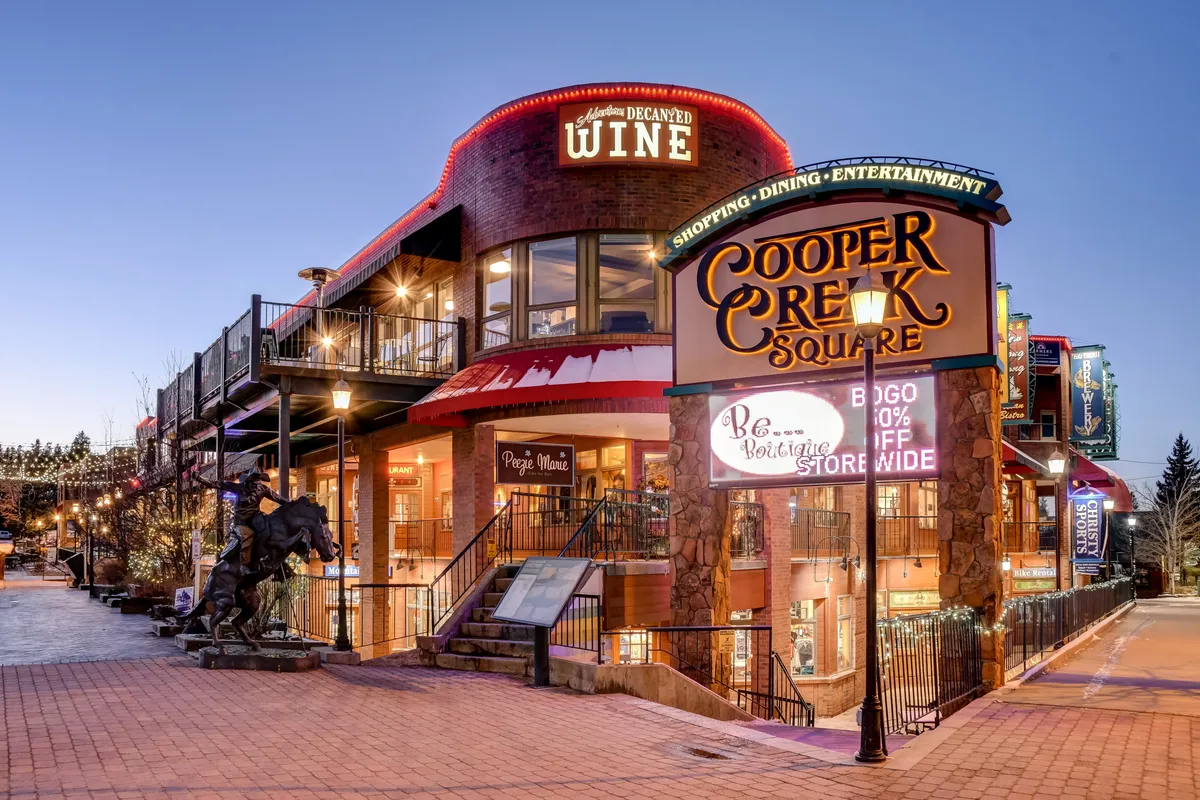 This exterior image showcases the Cooper Creek Square sign, a wine shop, an outdoor seating area, and a horse sculpture. The atmosphere is vibrant and lively, suggesting a community with plenty to explore. The presence of open-air spaces and nearby amenities emphasizes the property's proximity to outdoor attractions and pet-friendly gathering areas.